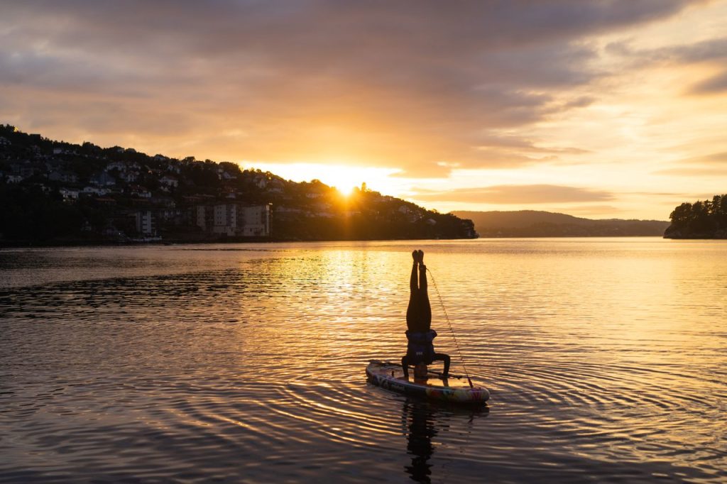 A peaceful sunset in Norway with a silhouette practicing headstand on a paddleboard.