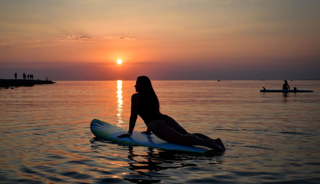 A woman enjoys paddleboarding during a vibrant summer sunset in Tallinn, Estonia.